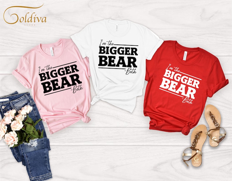 May include: Three t-shirts with the text "I'm the BIGGER BEAR - Beth" printed on them. The shirts are pink, white, and red.