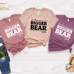 May include: Three t-shirts with the text "I'm the Bigger Bear - Beth" printed on them. The shirts are in different colors: pink, beige, and purple.