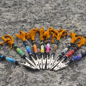 Può includere: Un set di dieci clip per capelli con perline colorate e un fiocco di pelle marrone. Le clip sono in metallo e hanno un meccanismo a molla. Le perline sono disposte in una varietà di motivi e colori, tra cui rosso, arancione, giallo, verde, blu, viola e nero.