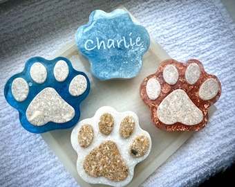 May include: Four resin paw print ornaments, two blue, one gold, and one white. The blue paw print has the name "Charlie" written on it.