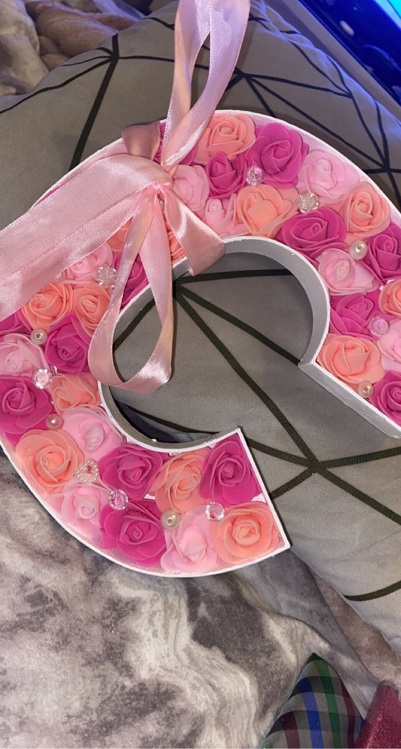 May include: A pink and peach letter C made of foam roses with a pink satin ribbon tied around it.