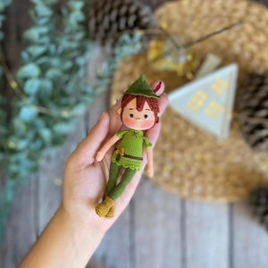 May include: A handmade crochet doll of a character wearing a green outfit and hat. The doll has brown hair and a tan face. The doll is approximately 13 cm tall. The doll is a whimsical, handcrafted item.
