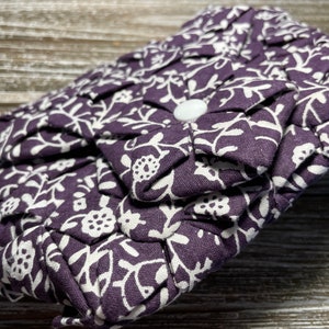 May include: A small purple fabric clutch with a white floral pattern. The clutch has a white button closure.