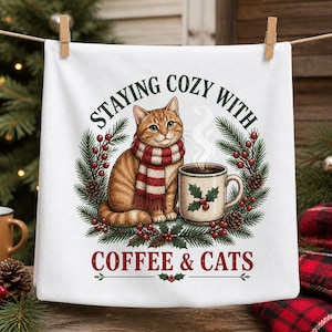 May include: A white kitchen towel featuring a graphic of an orange tabby cat wearing a red and white striped scarf next to a mug of coffee. The design includes pine branches, red berries, and the text "STAYING COZY WITH COFFEE & CATS".