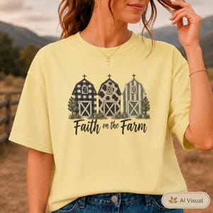 Może przedstawiać: Jasnoż&oacute;łty t-shirt z kr&oacute;tkim rękawem z grafiką przedstawiającą trzy stodoły w r&oacute;żnych wzorach: czarno-białą kratę, łaty krowie i zielone paski. Poniżej stod&oacute;ł znajduje się napis Faith on the Farm wykonany czarną, ozdobną czcionką.