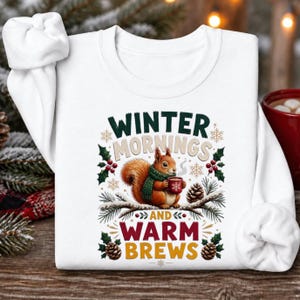 May include: A white long-sleeve sweatshirt featuring a graphic of a brown squirrel wearing a green scarf and holding a red mug. The text reads Winter Mornings and Warm Brews, surrounded by illustrations of pine branches, holly, and snowflakes.