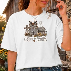 May include: A white t-shirt featuring a graphic print of a rustic barn, a cross, a windmill, and sunflowers, all topped with a leopard print bow. The text Sown in Faith is printed in a cursive script below the illustration of the farm buildings.