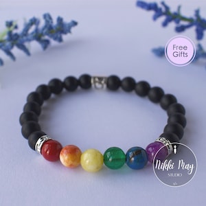 Peut inclure: Un bracelet en perles noires avec un arc-en-ciel de pierres colorées. Les pierres sont rouge, orange, jaune, verte, bleue et violette. Le bracelet est fait de perles noires mates et d'accents argentés. "Cadeaux gratuits" est écrit dans un cercle sur l'image.