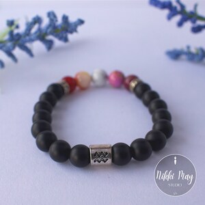 May include: Black beaded bracelet with a silver charm featuring the Aquarius zodiac symbol. The bracelet also has colorful beads in red, pink, white, and orange.