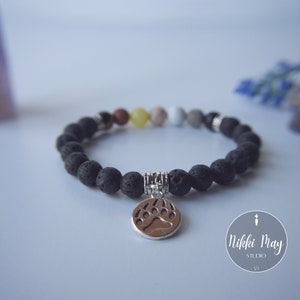 Puede incluir: Pulsera de cuentas de roca volc&aacute;nica negra con un dije de plata en forma de pata de oso. La pulsera tiene una variedad de peque&ntilde;as cuentas de colores intercaladas.