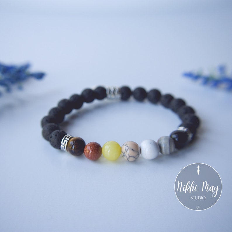 Puede incluir: Un brazalete de roca de lava negra con cuentas plateadas y cuentas de piedras preciosas de colores. El brazalete presenta cuentas de ojo de tigre, jaspe rojo, aventurina amarilla, howlite blanca y &oacute;nix negro.