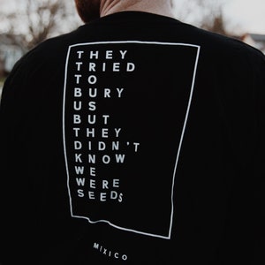 May include: Black t-shirt with white text in a rectangular frame. The text reads: "THEY TRIED TO BURY US BUT THEY DIDN'T KNOW WE WERE SEEDS." Below the text is the word "MIXICO."