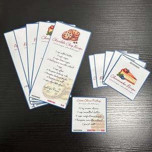 May include: A set of printable recipe cards with blue borders. The cards feature illustrations of chocolate chip cookies, cheesecake, and cream cheese frosting. The recipes are written in red and black text. The cards are labelled "CREATIVESPACES" and have a "SAVINGS GOAL" of £0.00.