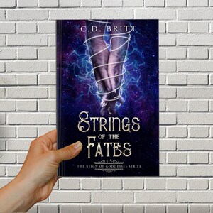 May include: Book cover with a dark blue background and a galaxy design. Two hands are intertwined with a white string. The title is "Strings of the Fates" with the subtitle "The Reign of Goddesses Series".