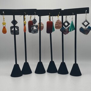May include: A set of eight unique earrings displayed on a black stand. The earrings feature geometric shapes and patterns in various colors, including red, orange, blue, and green.