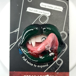May include: A green, glossy, open-mouthed design with fangs and a pierced tongue. The design is on a black background with the text "Snap better photos" and "Text with one hand". The bottom of the card reads "VEGAN LEATHER".