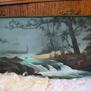 May include: A framed painting depicting a misty forest scene with a river flowing through it. The river has a waterfall and the trees are a dark green color. The painting is in a green frame.
