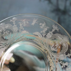 May include: Clear glass plate with intricate floral and foliate etched design around the rim. The etched details include stylized flowers, leaves, and delicate patterns, creating an elegant, vintage aesthetic.