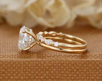 May include: A gold engagement ring set with a large oval-shaped center stone and a matching band with smaller stones. The ring is set on a brown background.