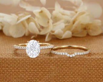 May include: A set of two gold engagement rings with a large oval-shaped center stone and a smaller band with a row of smaller stones. The rings are on a brown textured surface.