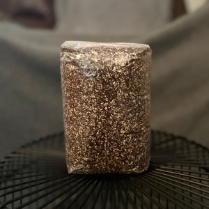 May include: A brown and white speckled block of substrate in a clear plastic bag. The substrate is sitting on a black wire rack.