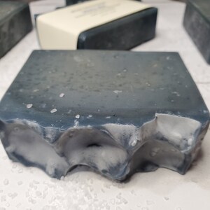 Peut inclure: Gros plan sur plusieurs pains de savon rectangulaires. Le savon est d'un gris bleu fonc&eacute; avec une surface textur&eacute;e et des accents blancs. Une barre a un bord rugueux et irr&eacute;gulier. Le savon semble avoir de petits cristaux blancs &agrave; la surface.