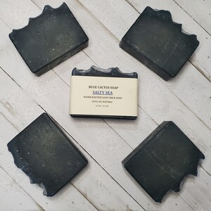 Peut inclure: Cinq savons carr&eacute;s gris fonc&eacute; avec un bord textur&eacute; unique sont dispos&eacute;s sur une surface claire &agrave; grain de bois. Le savon central est &eacute;tiquet&eacute; "Blue Cactus Soap Salty Sea", savon artisanal au lait de ch&egrave;vre.