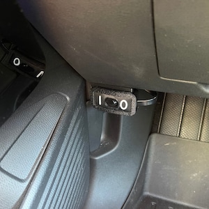 May include: A black plastic switch with a white "1" and "0" on it. The switch is mounted in a car's interior.