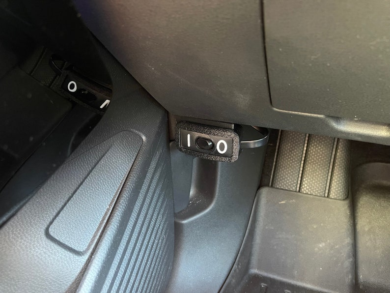 May include: A black plastic switch with a white "1" and "0" on it. The switch is mounted in a car's interior.