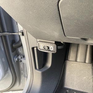 May include: A black plastic switch with a white label that says "1 0" is mounted on the side of a car's interior. The switch is located near the door hinge.