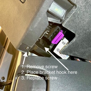 May include: A close-up of a black plastic panel with a screw and a purple connector. The text on the panel reads: "1. Remove screw 2. Place bracket hook here 3. Replace screw".