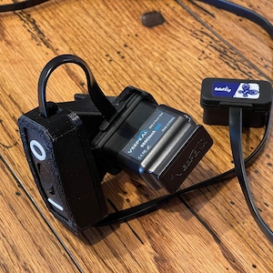 May include: A black OBD2 adapter with a black strap and a small black box with a blue label that says "barfly". The adapter has the text "VEEPEAK OBDCheck BLU" on it.