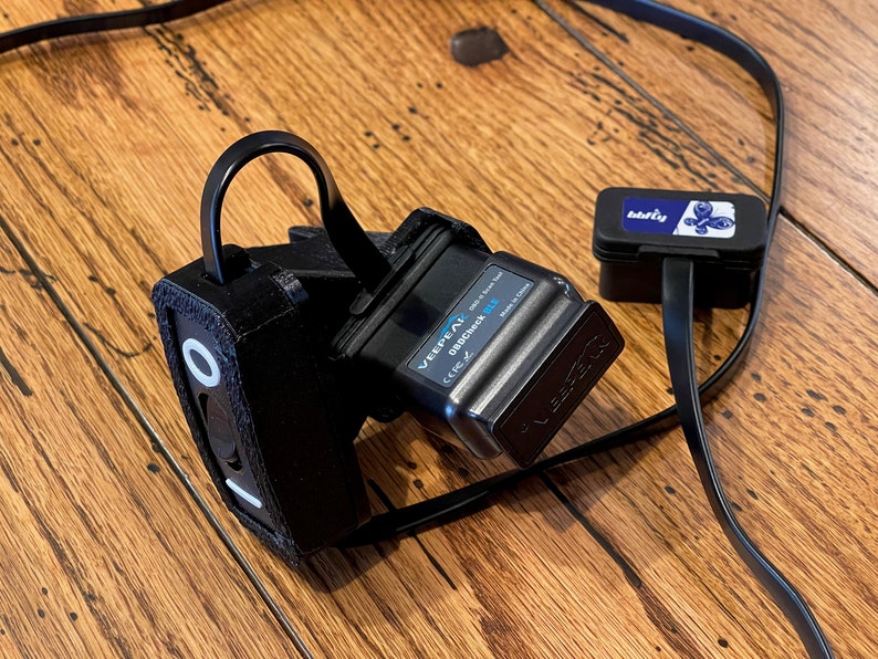 May include: A black OBD2 adapter with a black strap and a small black box with a blue label that says "barfly". The adapter has the text "VEEPEAK OBDCheck BLU" on it.