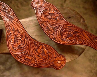 May include: Two brown leather straps with intricate floral designs, possibly for a cowboy boot or other leather goods.