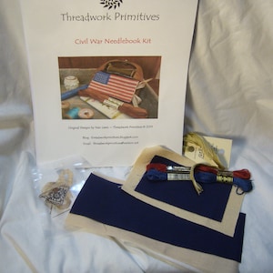 May include: A Civil War Needlebook Kit by Threadwork Primitives. The kit includes a printed pattern, fabric, and embroidery floss. The pattern features a small American flag.