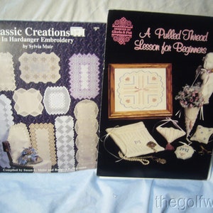 May include: Two books on embroidery techniques. The book on the left is titled "Classic Creations in Hardanger Embroidery by Sylvia Muir". The book on the right is titled "A Pulled Thread Lesson for Beginners".