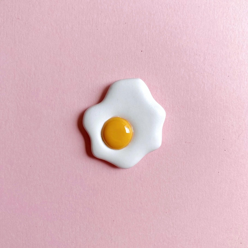 A sunny-side-up fried egg on a soft pink background. The egg yolk is glossy, which lends to its realism. A great gift for a food-lover/foodie/cook.