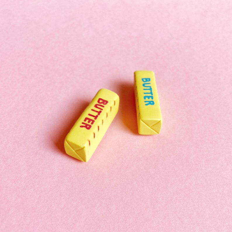 Two small, pale yellow butter stick magnets showcasing the ends of the sticks with wrapper fold details.