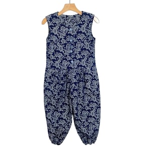 May include: A sleeveless blue jumpsuit with a white floral pattern. The jumpsuit has a button-up front and a relaxed fit.