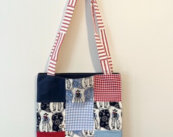 May include: A patchwork tote bag featuring navy, red polka dots, blue gingham, and a cowboy print. The handles are red and white striped. The bag is suspended from a gold heart-shaped hook.