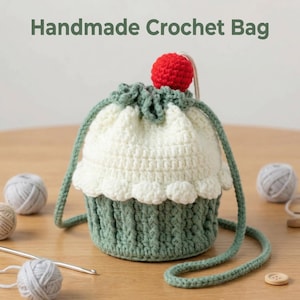 May include: Handmade crochet bag in the shape of a cupcake. The bag is white and green with a red cherry on top. The bag has a drawstring closure and a green strap. The text "Handmade Crochet Bag" is at the top.