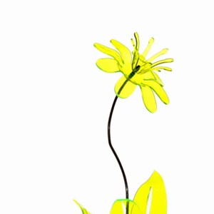 May include: A decorative, neon yellow flower sculpture with a black stem and a base. The flower has multiple petals and is set against a white background. The sculpture's leaves are also neon yellow.