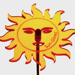 May include: Orange and red sun-shaped cake topper with a smiling face and the text "Sun-Glowz".