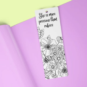 May include: A white bookmark with black ink featuring a floral design and the text "She is more precious than rubies."