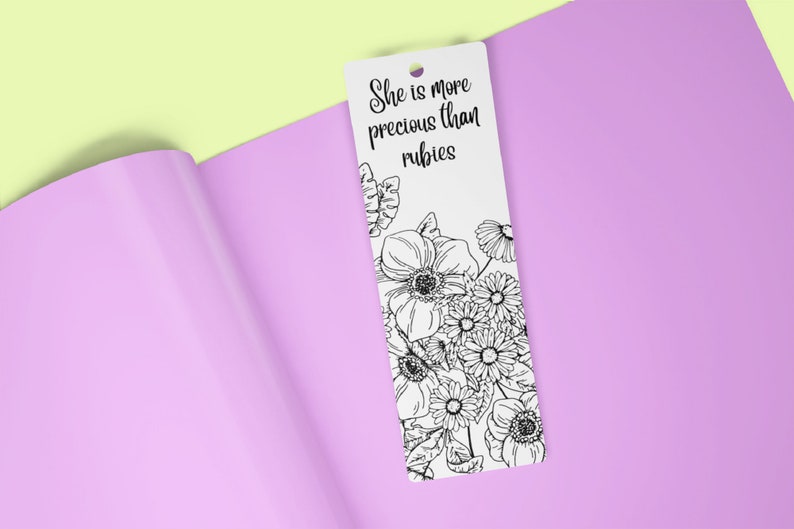 May include: A white bookmark with black ink featuring a floral design and the text "She is more precious than rubies."