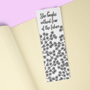 May include: White bookmark with a black floral pattern and the text "She laughs without fear of the future".