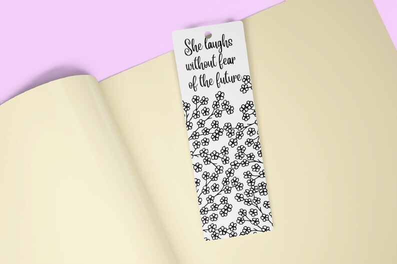 May include: White bookmark with a black floral pattern and the text "She laughs without fear of the future".