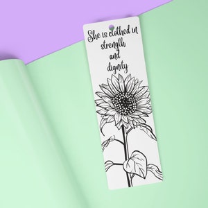 May include: A white bookmark featuring a black and white illustration of a sunflower. The text "She is clothed in strength and dignity" is printed on the bookmark.