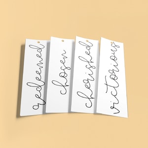 May include: Four white bookmarks with black handwritten text. The text on the bookmarks reads "redeemed", "chosen", "beginished", and "victorious".