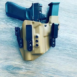 May include: A tan leather holster with a black gun inside. The holster has multiple black clips and a black strap.